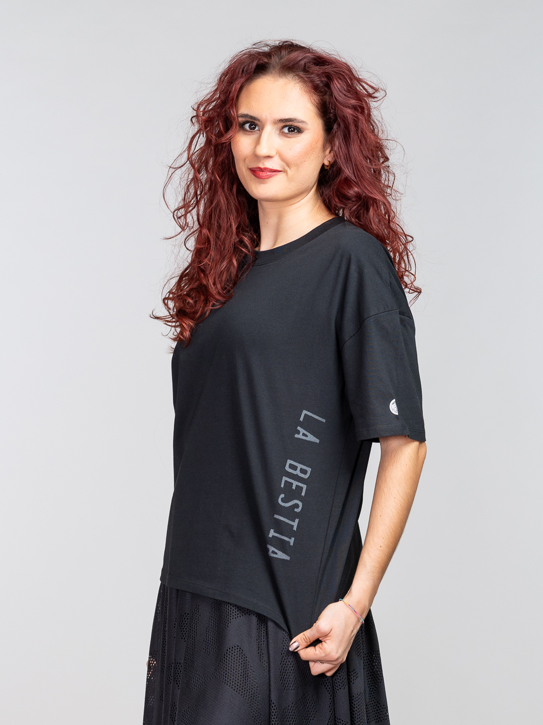 Crna oversized majica s vertikalnim srebrno-sivim natpisom "LA BESTIA" na bočnoj strani.