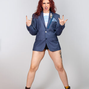 Djevojka s crvenom kosom u energičnoj pozi nosi plavi upcycled sako ukrašen plavom čipkom i nizom unikatnih gumba na reveru.