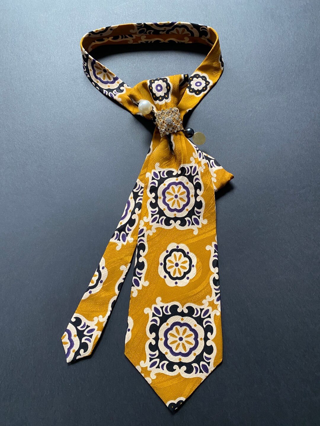 Unikatna svilena ženska kravata u senf žutoj boji s cvjetno-geometrijskim uzorkom ukrašena brošem i iglom
