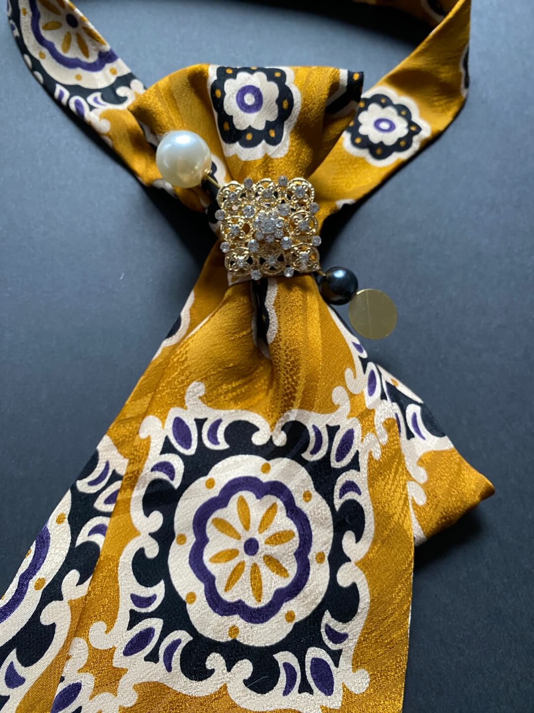 Unikatna svilena ženska kravata u senf žutoj boji s cvjetno-geometrijskim uzorkom ukrašena brošem i iglom