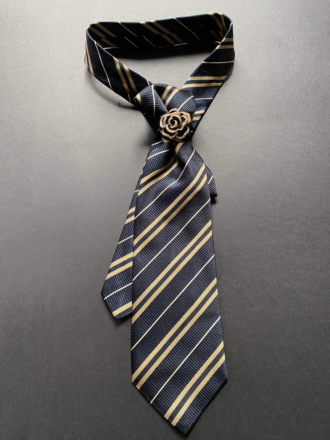 Svilena crna ženska kravata sa zlatnim prugama ukrašena brošem u obliku ruže