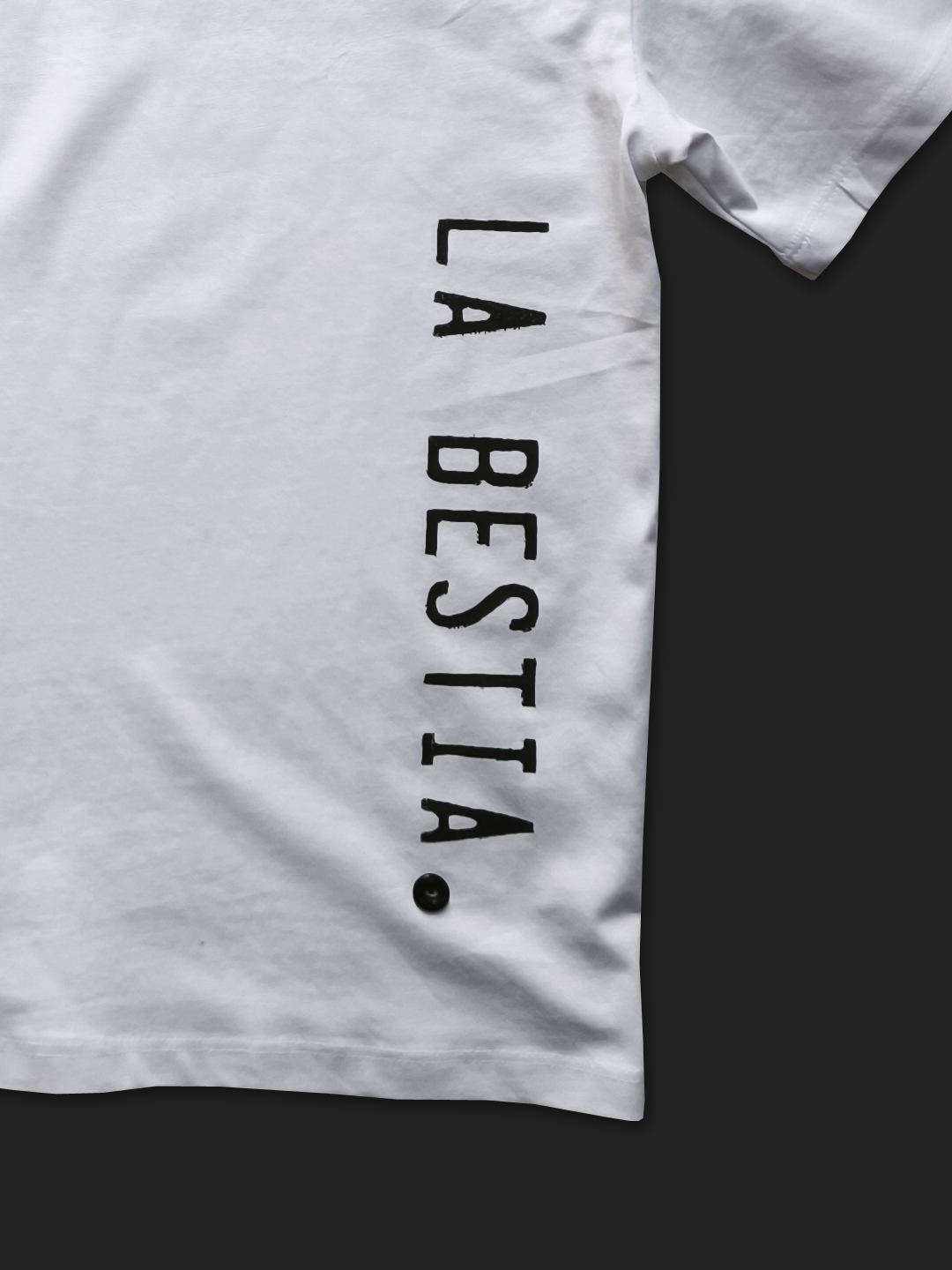 Bijela oversized majica s vertikalnim srebrno-crnim natpisom "LA BESTIA" na bočnoj strani.