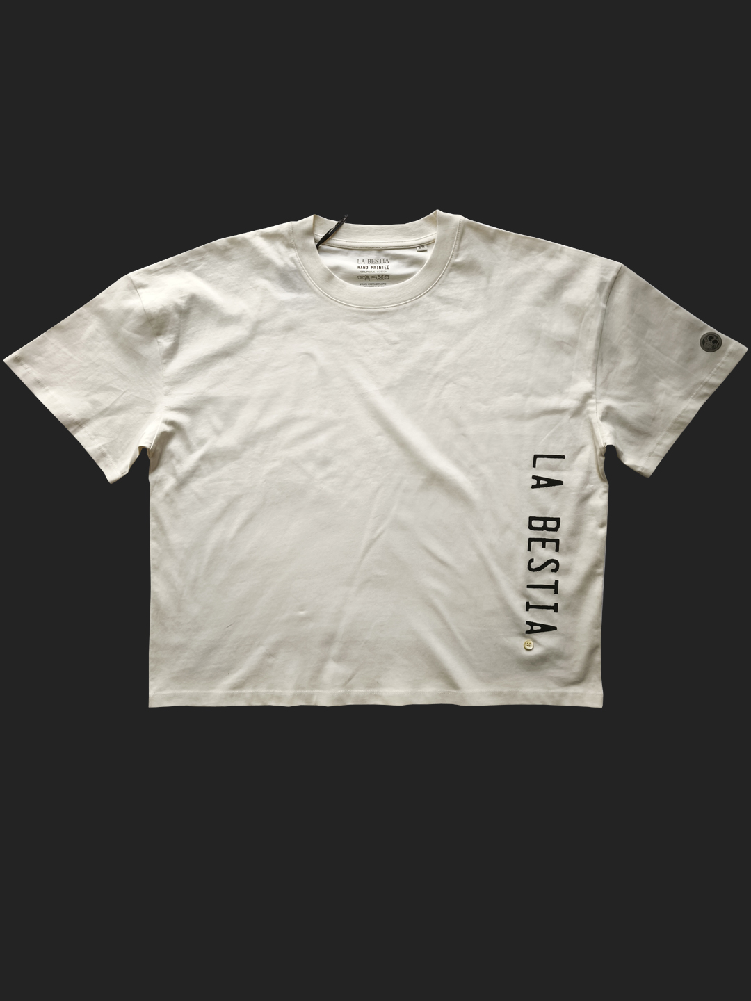 Prljavo-bijela oversized majica s vertikalnim srebrno-sivim natpisom "LA BESTIA" na bočnoj strani.